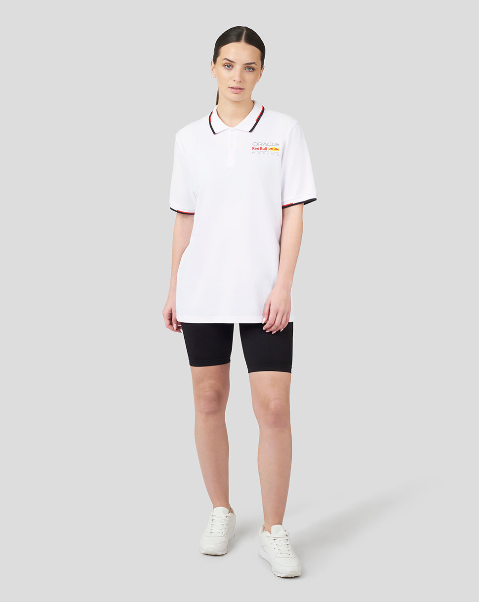Female model in white Oracle Red Bull Racing Core Polo with left chest logo and black shorts.
