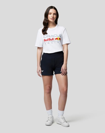 Female model in white Oracle Red Bull Racing front logo T shirt with navy shorts and white sneakers.